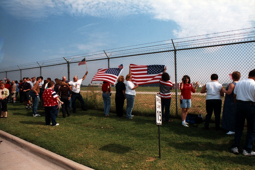 Employees at Southwest Headquarters gather along the runway security fence at Dallas (Love Field), holding banners and waving American flags as they watch the first Dallas flights takeoff on Sept. 14, 2001.